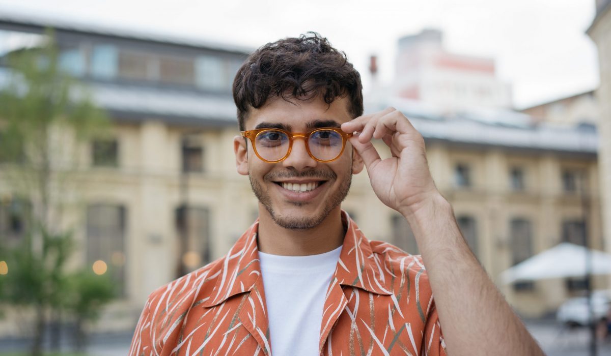 Portrait d'un bel homme indien souriant portant des vêtements décontractés, des lunettes hipster, regardant la caméra, debout dans la rue