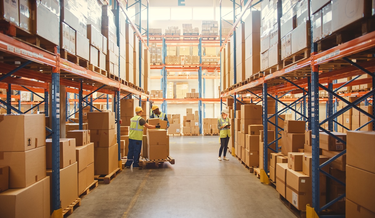 Entrepôt et ses rayonnages avec des marchandises dans des boîtes en carton, des employés qui scannent et trient les paquets, les déplacent avec des transpalettes et des chariots élévateurs. Centre de distribution des produits dans le commerce de détail.